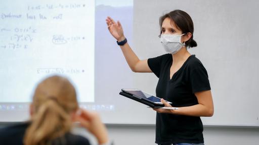 professor teaching with face mask on and a student (out of focus) in the bottom, right corner